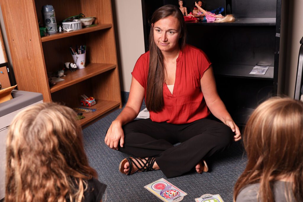 A therapist sits down on the floor to talk at the same level with two children.